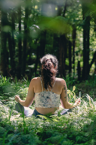 Young woman sitting in the grass while meditating in the wilderness. Vertical