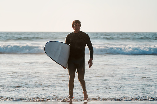 latin surfer getting out of the water with his board after surfing at sunset