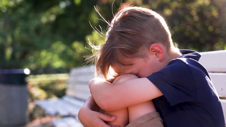 Crestfallen Crying child boy sitting on a bench covering his face