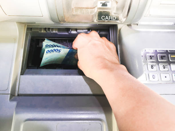 A man's hand is in the process of withdrawing hundreds of thousands of rupiah from an ATM machine stock photo