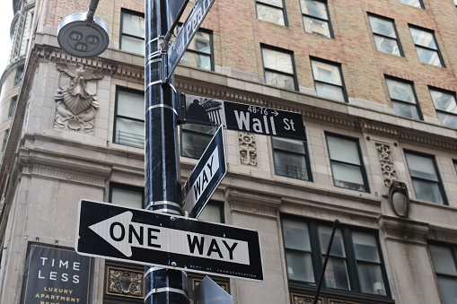 Manhattan, New York City, USA - May 17, 2022 - Street signs in the Financial District showing the direction to Wall Street and a one way arrow.