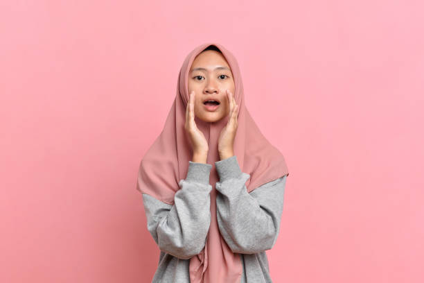 Young Muslim woman with gray sweater shouting with mouth open Young Muslim woman with gray sweater over isolated pink background shouting with mouth open speaking with forked tongue stock pictures, royalty-free photos & images