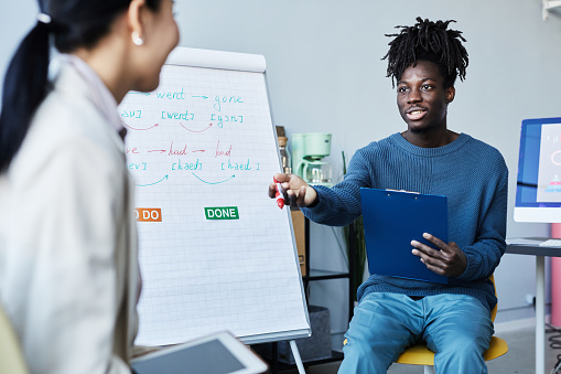 Portrait of young black man leading group discussion during English class in office