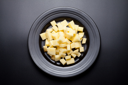 Chopped raw potatoes in a black plate on black background. Top view.
