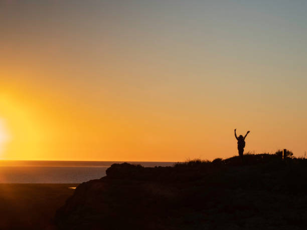istock Distant person in silhouette standing on rock at sunset 1400525363