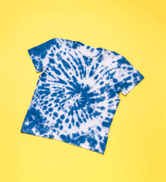 istock Blue T-shirt with a spiral pattern in tie dye style on a yellow background. Flat lay. 1400528976