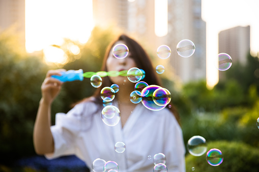 young woman blowing soap bubbles at sunset