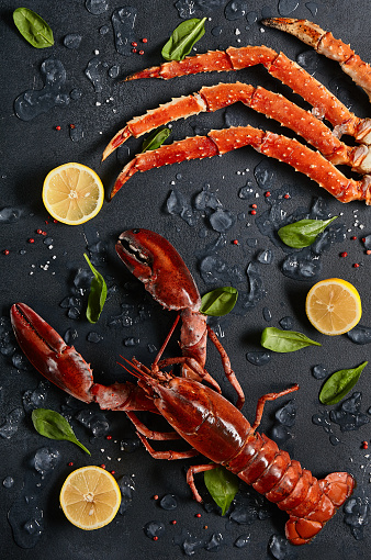 Lobster and crab legs with ice and lemon on dark background top view. Delicatessen crab and lobster seafood on black slate table. Crustacean seafood aesthetics. Luxury food - alive lobster and crab legs