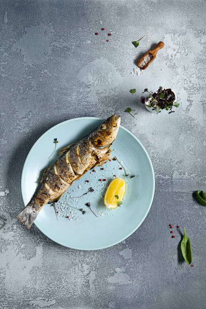 직물로 돌 배경에 파란색 접시에 구운 해저. 레스토랑 메뉴 개념에서 생선 구이. 레몬과 함께 구운 무지개 송어. 현대 해산물 메뉴. 지중해 음식. - trout prepared fish whole grilled 뉴스 사진 이미지