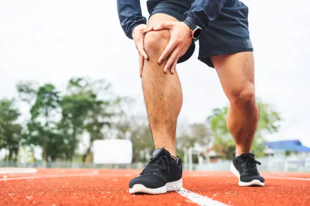 Young man runner has sore knee because he ran too long. Male Exercising until the injury. Overtrained. Young sport man accident running on track