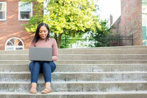 College student is outside using laptop to study on university campus