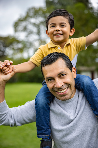 Portrait of a happy Latin American father carrying his son on his shoulders and smiling