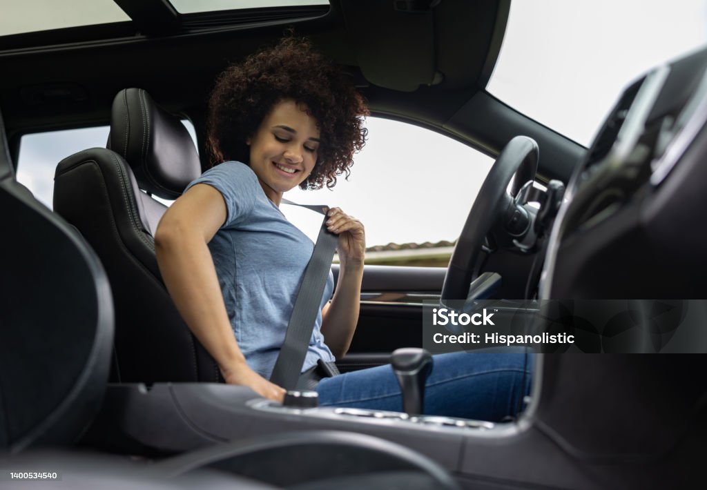Female driver fastening her seat belt in her car Happy Latin American female driver fastening her seat belt in her car and smiling - safety concepts Seat Belt Stock Photo