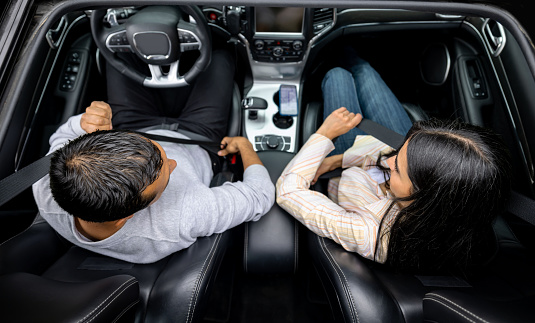 Happy Latin American couple going on a road trip in their car and fastening their seat belts - safety concepts