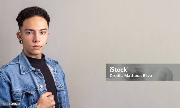 Young Brazilian Man With Wouldbe Face Wearing A Denim Jacket On Gray Background With Copy Space Stock Photo - Download Image Now