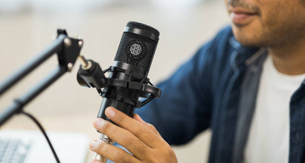istock Close-up content creator man host streaming a podcast on laptop set up with headphones and condenser microphone interview guest conversation at broadcast studio. Blogger recording voice over radio 1400535611