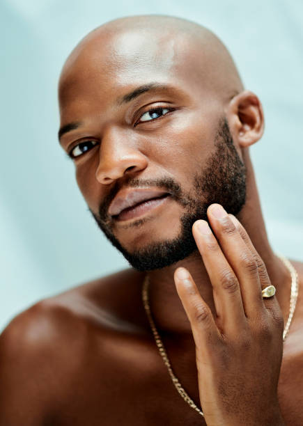 istock A bald African model touching his face and looking at the camera. He has a ring on his finger and a beard. The necklace his wearing is gold 1400536605