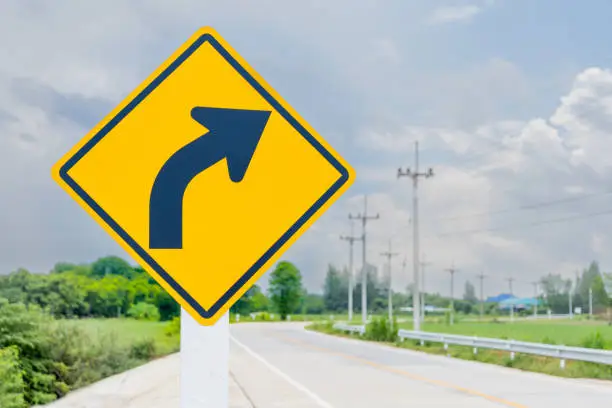 The new symbol reflective yellow right turn sign has a black arrow inside the frame located on the side of the country road. safety information transport roadside