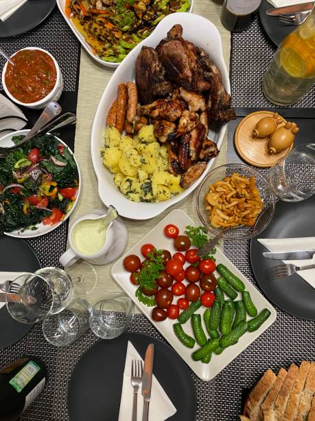 The table is set for a friendly party, dishes with snacks and bottles of drinks, people's hands in the frame. View from above