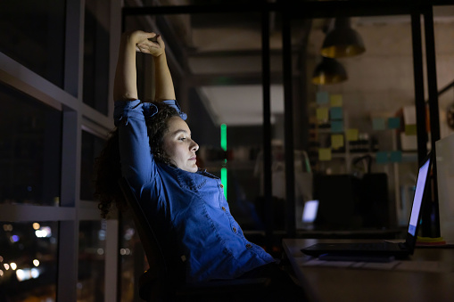 Latin American woman stretching on her desk while working late at the office