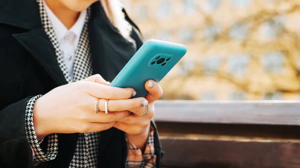 istock Caucasian woman chatting, browsing internet on mobile phone while sitting onbench on sunny day. Close-up woman's hands use smartphone outdoors, copy space. Selective focus on phone 1400544898