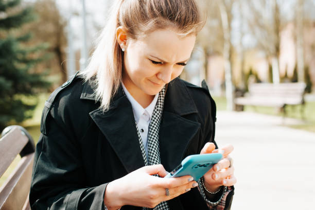 istock Concentrated young woman using smartphone, browsing messages or news outdoors on sunny day. Close-up of pretty woman looking into mobile phone while sitting on park bench. Selective focus on face 1400544913