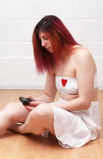 Young woman sitting on the floor, thinking about her broken heart with a gun in her hand
