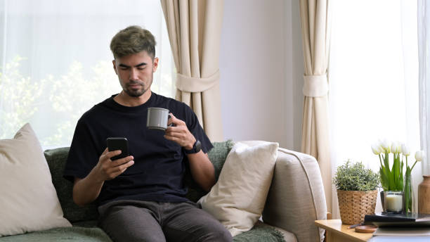istock Young man sitting on comfortable sofa and using smart phone, enjoying leisure weekend time at home. 1400556534