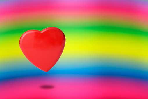 Red heart shaped metal floating in mid-air against rainbow background with copy apace.