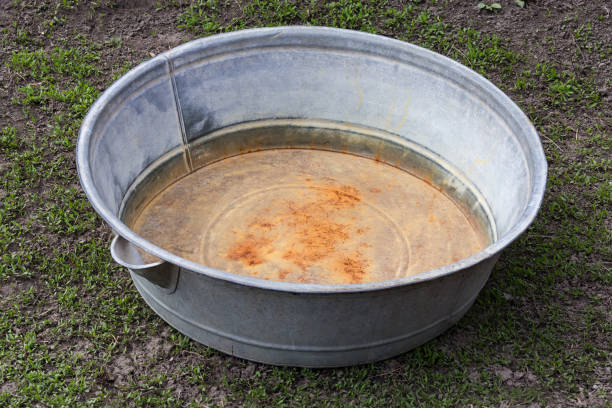 Empty old big round partly rusty washtub made with galvanized iron on the ground overgrown with fine grass
