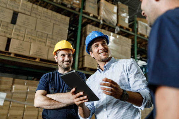 istock Happy inspector using digital tablet and talking to warehouse workers in a storage room. 1400560760