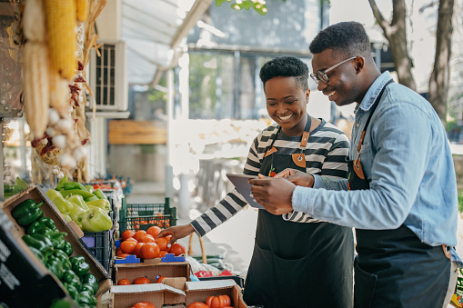 Two african american colleagues working in the fruit and vegetable store checking digital tablet