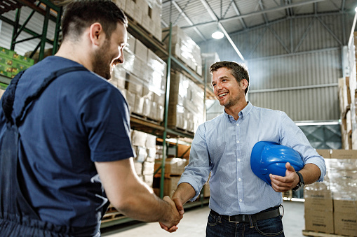 Happy inspector shaking hands with manual worker at distribution warehouse.