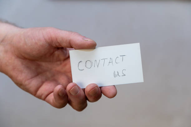 Contact us. Words written in jagged letters. A man's hand holds a white paper rectangle with text against a gray background.