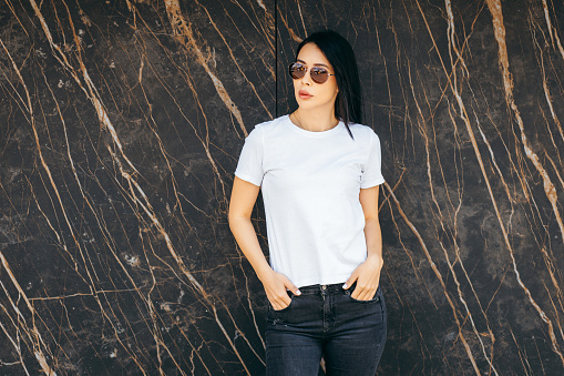 Stylish brunette asian girl wearing white t-shirt and sunglasses posing against street , urban clothing style. Street photography