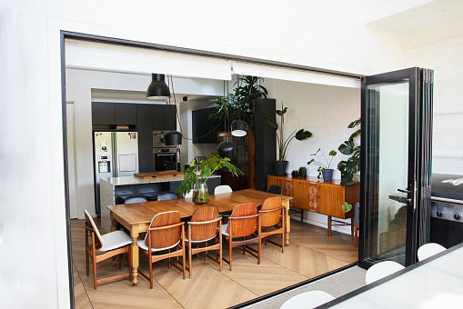 Table and chairs in an open plan dining area of a home next to the open doors of a sunny patio