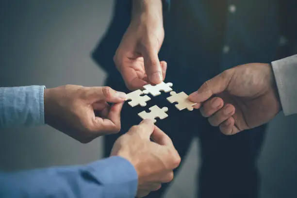 Photo of Concept of teamwork and partnership. Hands join puzzle pieces in the office. business people putting the jigsaws team together.Charity, volunteer. Unity, team business.