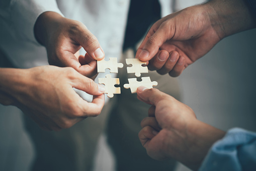 hand holding jigsaw piece with background of teamwork people connection