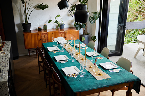 Dining table set with cutlery, plates and wine glasses in preparation for a dinner party in a friend's home