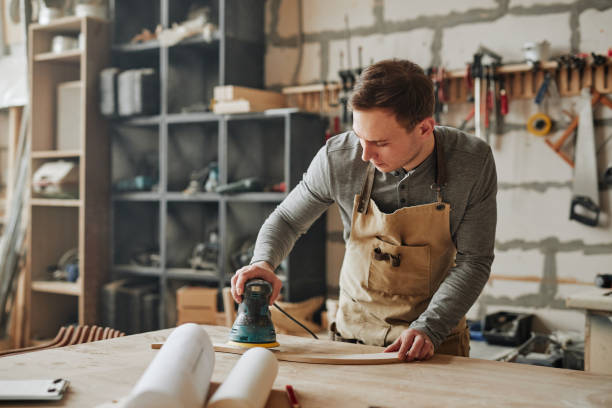 Young Man in Carpentry Workshop Warm toned portrait of young carpenter sanding wood and building handmade furniture piece in workshop, copy space woodshop stock pictures, royalty-free photos & images