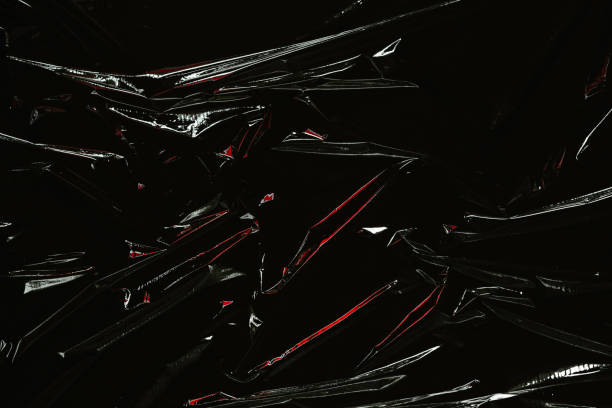 istock Transparent plastic wrap on black background. Crumpled wrinkled plastic cellophane. Reflecting red color light and shadow on creases and folds in plastic surface. Texture overlay effect template 1400570324