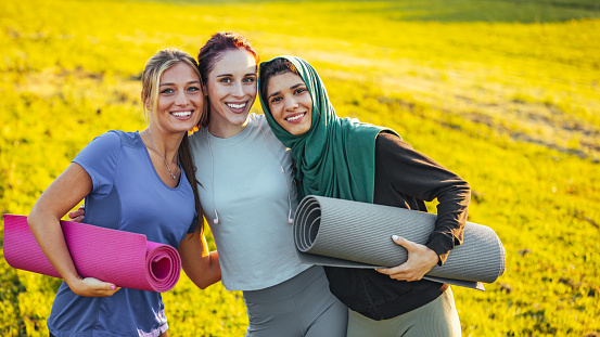 Portrait of cheerful fit young woman standing arms around each other in park. Multi-ethnic friends are wearing sports clothing. They are representing healthy lifestyle.
