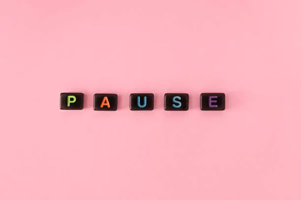 Pause button concept. Black beads on trendy pink background making word. Lifestyle phrase made of small letters symbolizing relax and keep calm