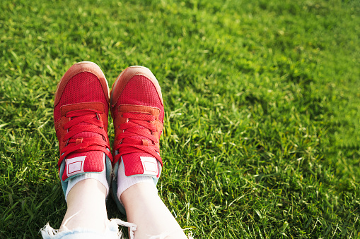 Woman sits on the grass, female legs in red sneakers on a background of green grass