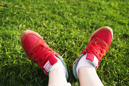 Woman sits on the grass, female legs in red sneakers on a background of green grass