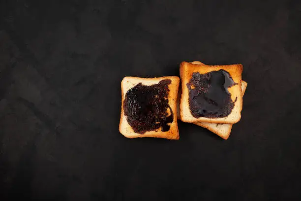 Photo of Hot toasted bread for breakfast. Roasted Aussie savory toasts with vegemite spread. Vegemite is a very popular yeast based spread in Australia. Dark background, copy space
