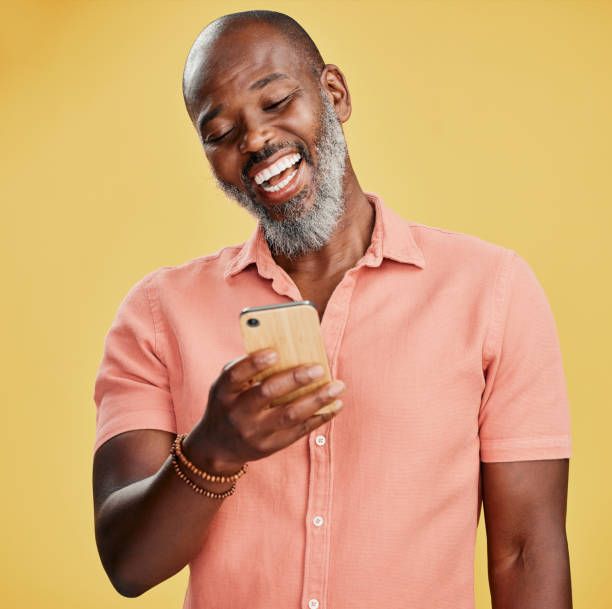 istock One happy African American man standing against a yellow studio background, holding and using his cellphone to browse the internet. Smiling black man laughing while browsing his phone for social media 1400577236