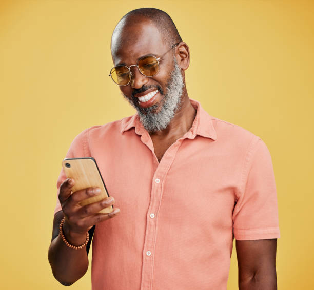 istock One mature african american using his phone while standing in studio isolated against a yellow background. Handsome man with a beard and wearing glasses reading and sending text message on his mobile 1400577239