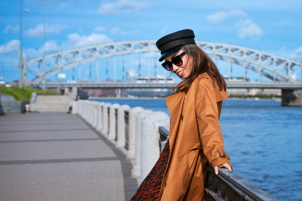 istock Beautiful woman in a cap and jacket posing while standing on the embankment 1400577301