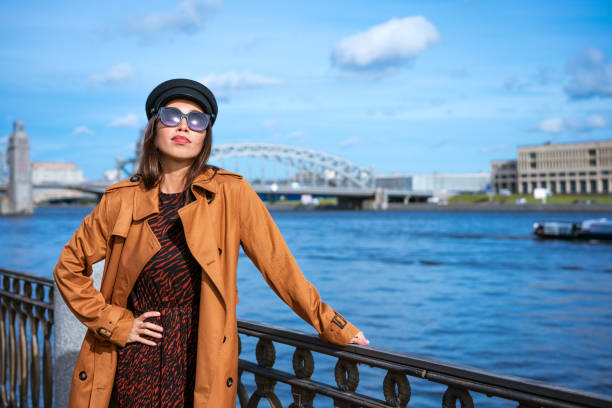 istock Beautiful woman in a cap and jacket posing while standing on the embankment 1400577307